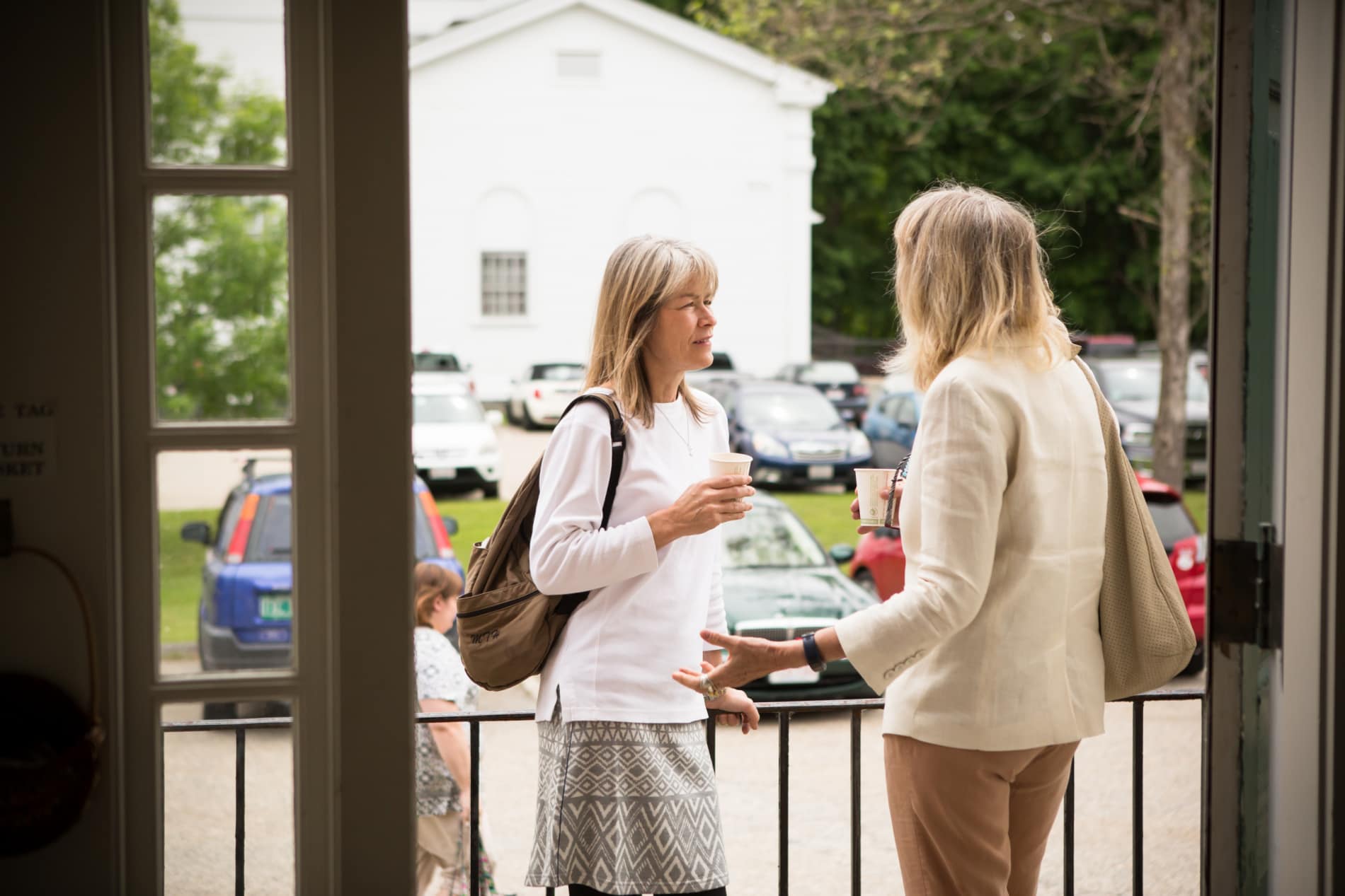 Two women drink coffee and talk at the entrance to the Stockbridge Congregational Church