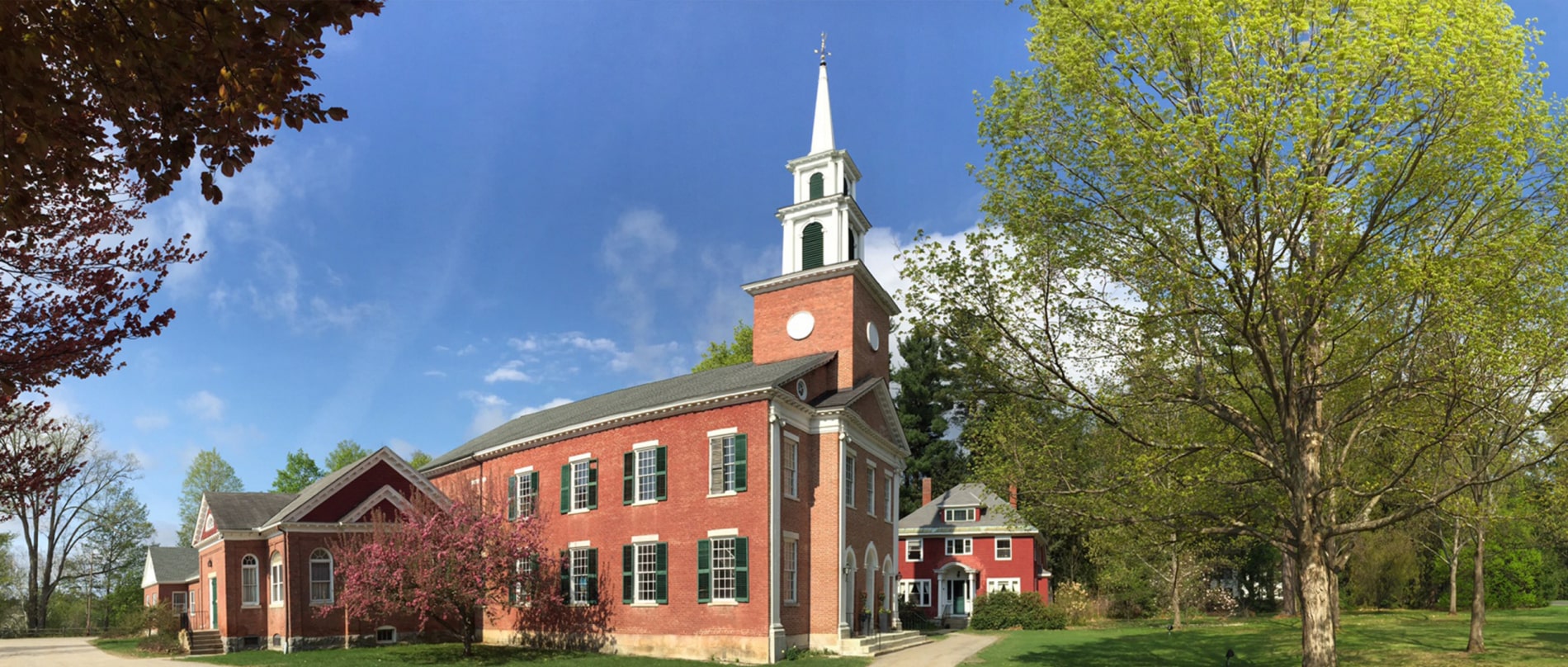 Exterior image of the historic 1824 congregational church in Stockbridge. A brick building with green shutters and a tall white steeple.