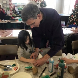 An older man demonstrates to a young girl how to stamp paint with a homemade potato stamp