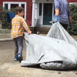 A young boy helps haul a tarp with leaves