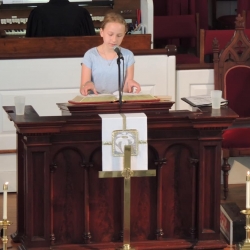 A preteen girl reads from the pulpit