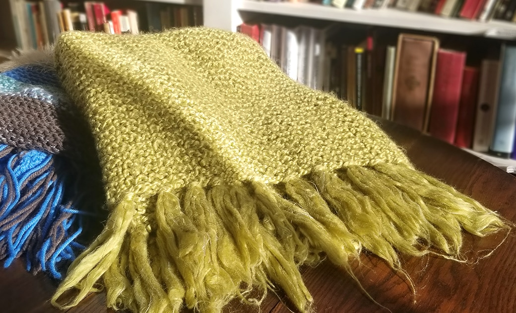 A green prayer shawl and a blue prayer shawl on a wooden table