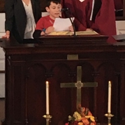 A boy reads scripture from the pulpit while his parents look on