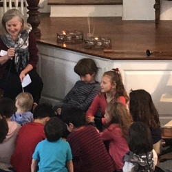 A woman offers the Children's Sermon on helping others to a group of children.