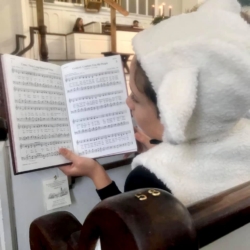 A boy dressed as a sheep sings from a hymnal