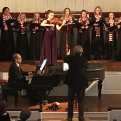 A young women's choir is accompanied by a violist