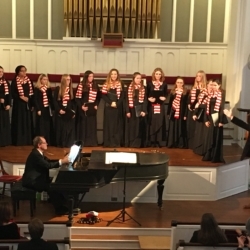 A young women's choir singing while a pianist plays.