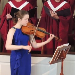 A young woman plays the viola while the choir sings