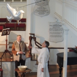 A dove-shaped balloon floats over a man playing Jesus, to symbolize the Holy Spirit