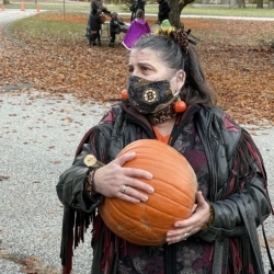 A woman dressed as a cat holds a pumpkin