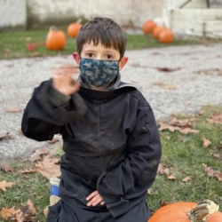 A boy in costume waves while decorating his pumpkin